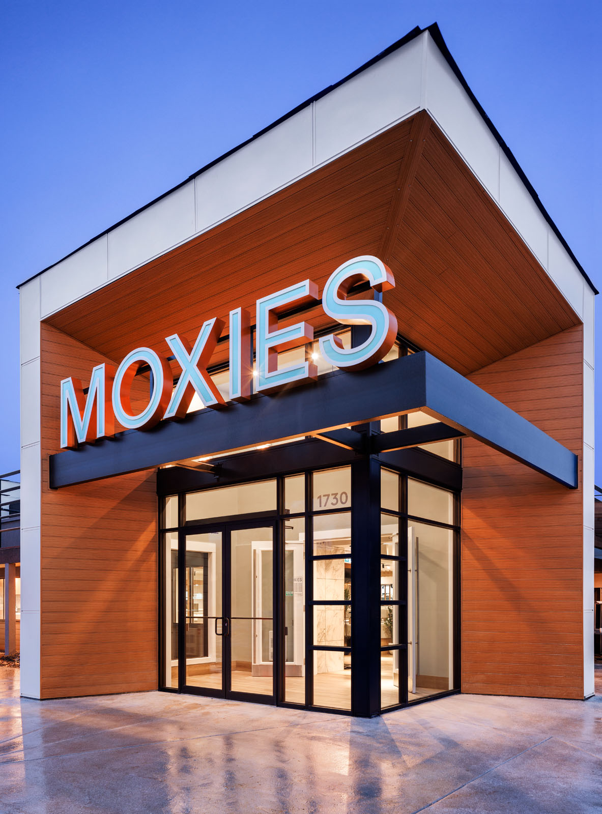 Architectural Exterior of New Moxies Restaurant Photographed at Dusk. Front Entrance With Light Spilling Out Past Moxies Sign.