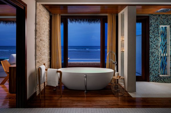 Sandals Royal Caribbean overwater villa of bathtub at night with towel hanging on rack and view to ocean