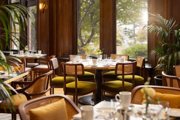 The Bengal Room at the Fairmont Empress in Victoria. Warm soft sunlight spills in through a window with gardens in the background onto a set round table with other tables soft in the foreground.