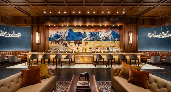 Old Hickory Restaurant inside the Gaylord Rockies Resort in Denver. Two couches in the foreground with the sprawling restaurant bar in the background with antler chandeliers and a dramatic mural depicting bison in the old west hangs on the wall behind the bar.